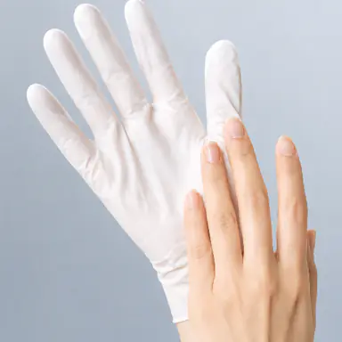A hand in a white moisturizing glove beside a bare hand, against a soft blue-gray background.